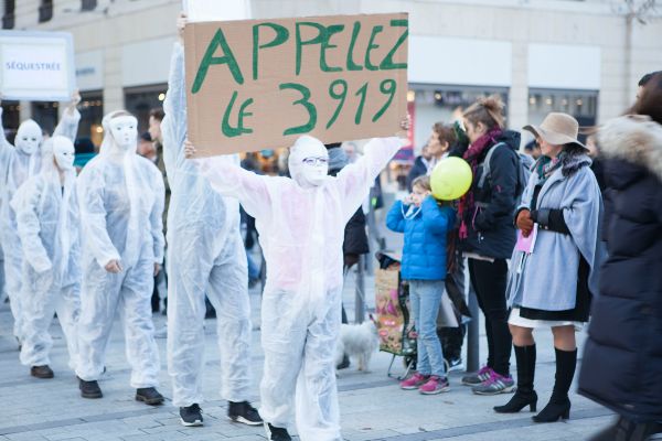 Manifestantes en combinaison blanche et masque blanc, avec une pancarte « Appelez le 3919 », lors d’une action contre les violences faites aux femmes