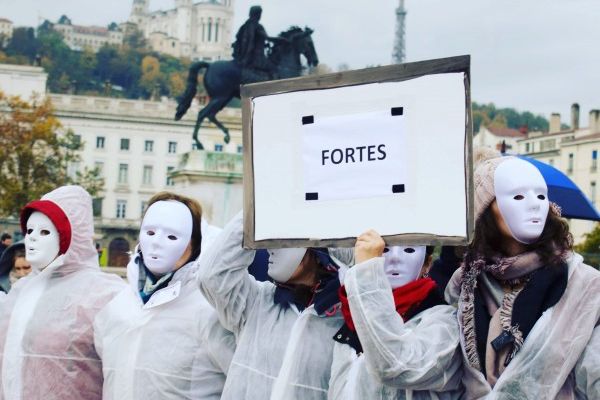 Militantes masquées de blanc avec une pancarte « Fortes », place Bellecour à Lyon, devant la statue équestre